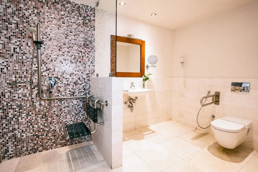 Accessible bathroom with mosaic tiled shower, grab bars, sink, and modern toilet in a spacious layout.