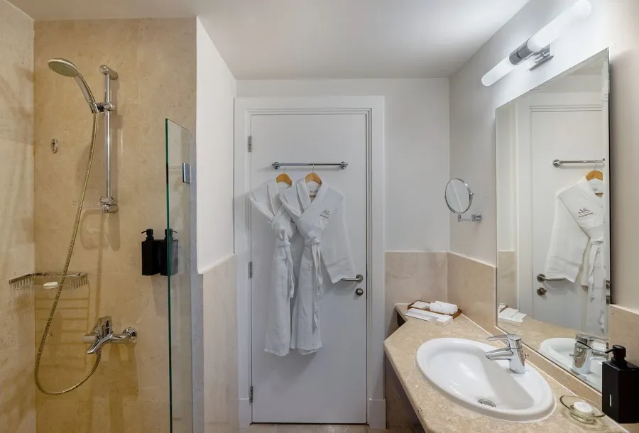 Modern bathroom featuring a glass shower, sink, and neatly hung white bathrobes.