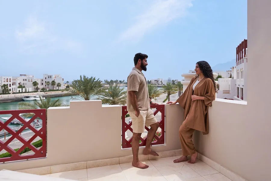 A couple on a balcony at Sifawy Boutique Hotel, overlooking a scenic waterfront and palm trees.